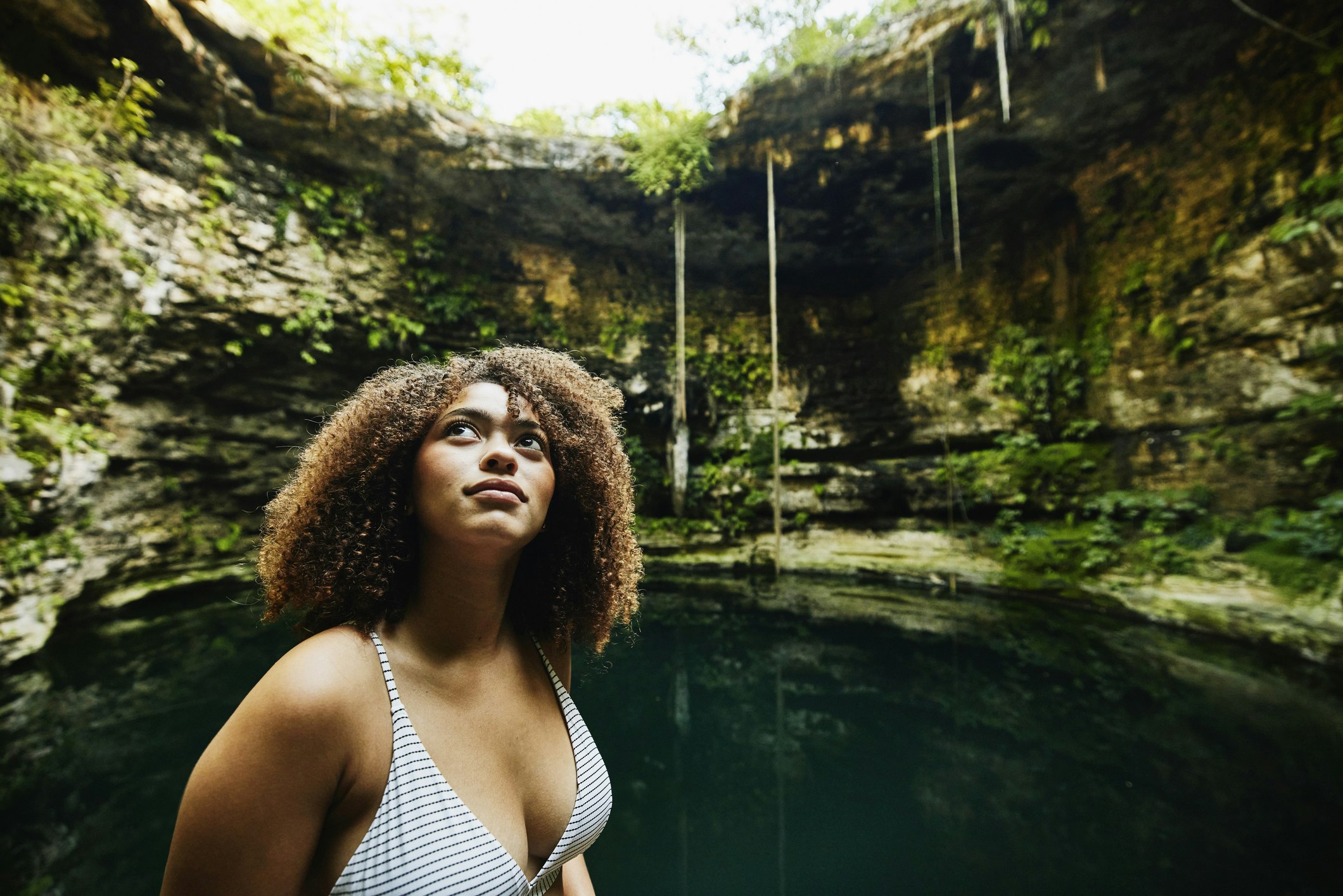 A woman standing near a cenote, a subterranean swimming hole, looking up at the natural walls around her in Mexico